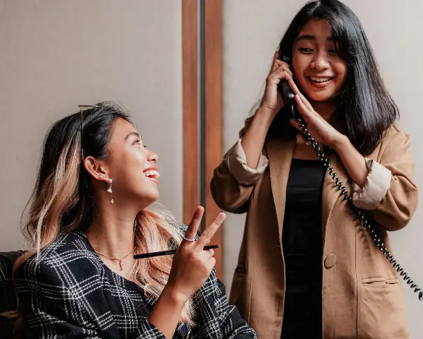 Persona conversando por telefono mientras consulta con su compañera de trabajo